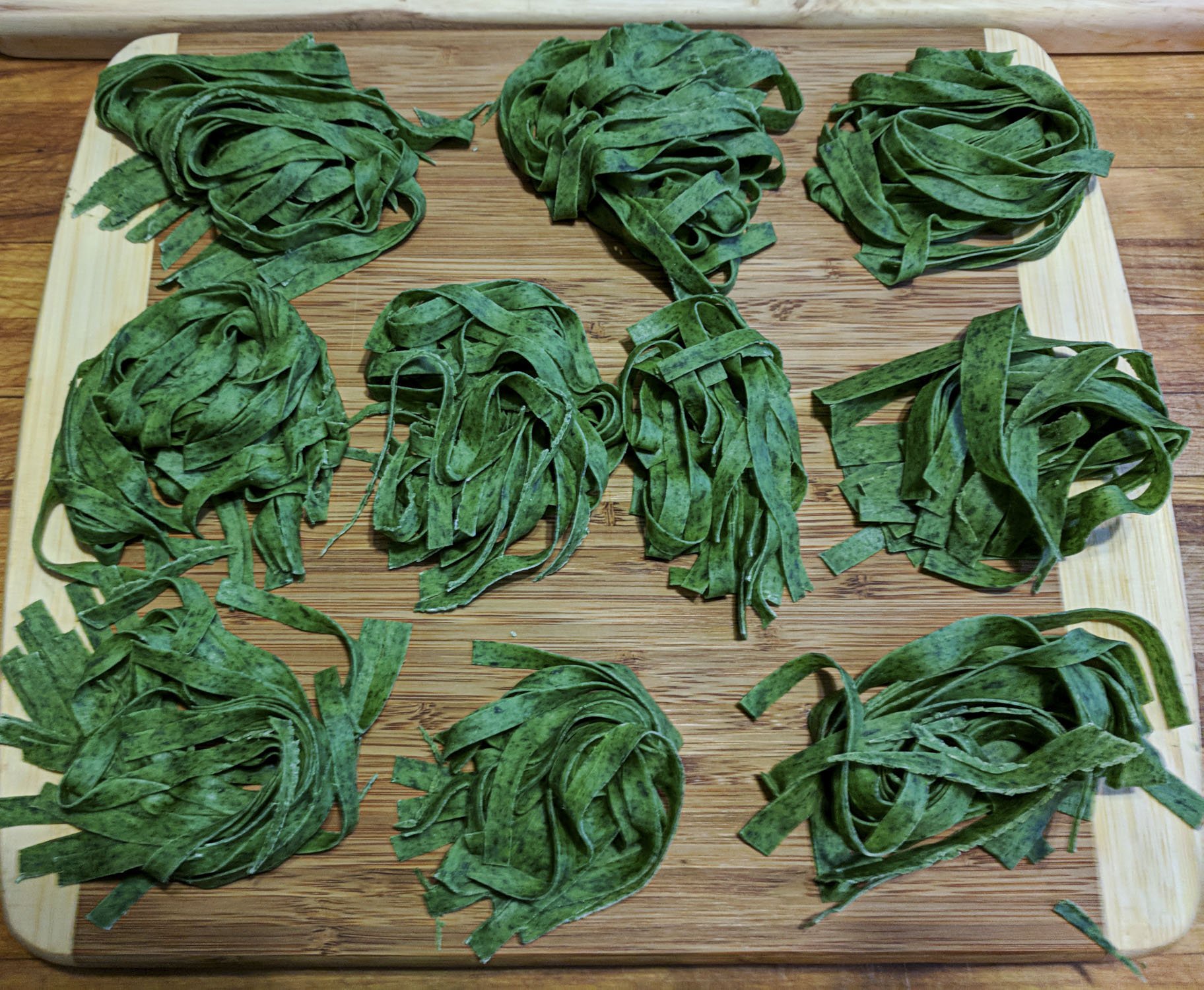 Green pasta curled on a wood cutting board