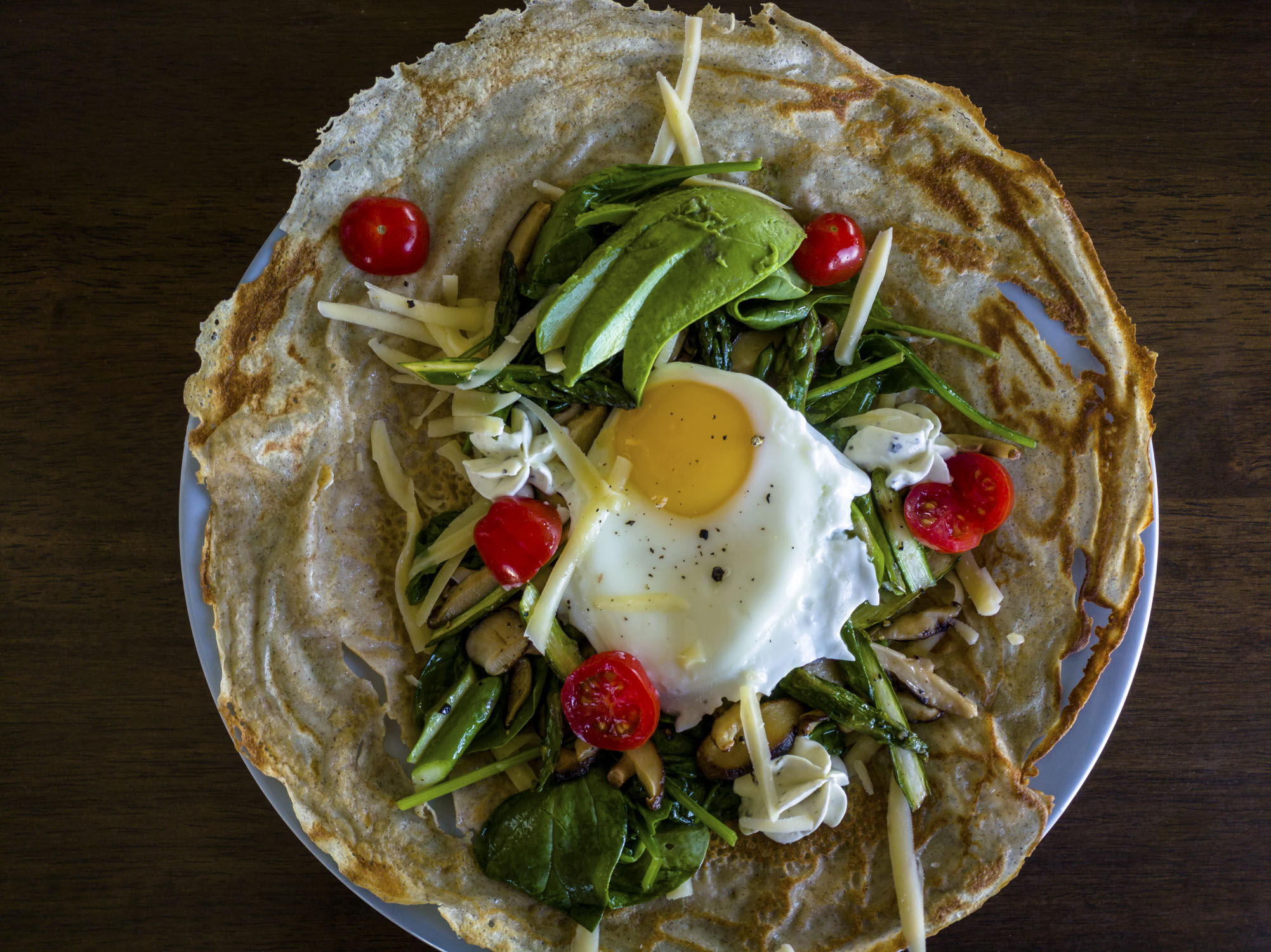 A crepe with greens, avocado, tomato, egg, and cheese